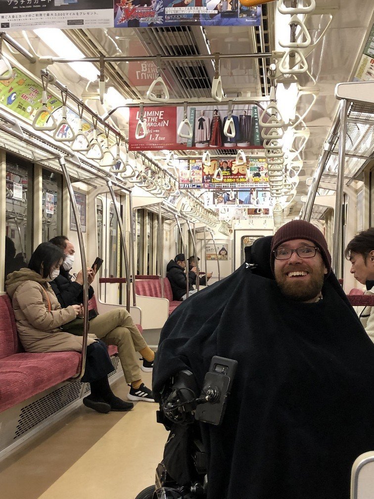A man in a power wheelchair travelling on a metro train in Japan
