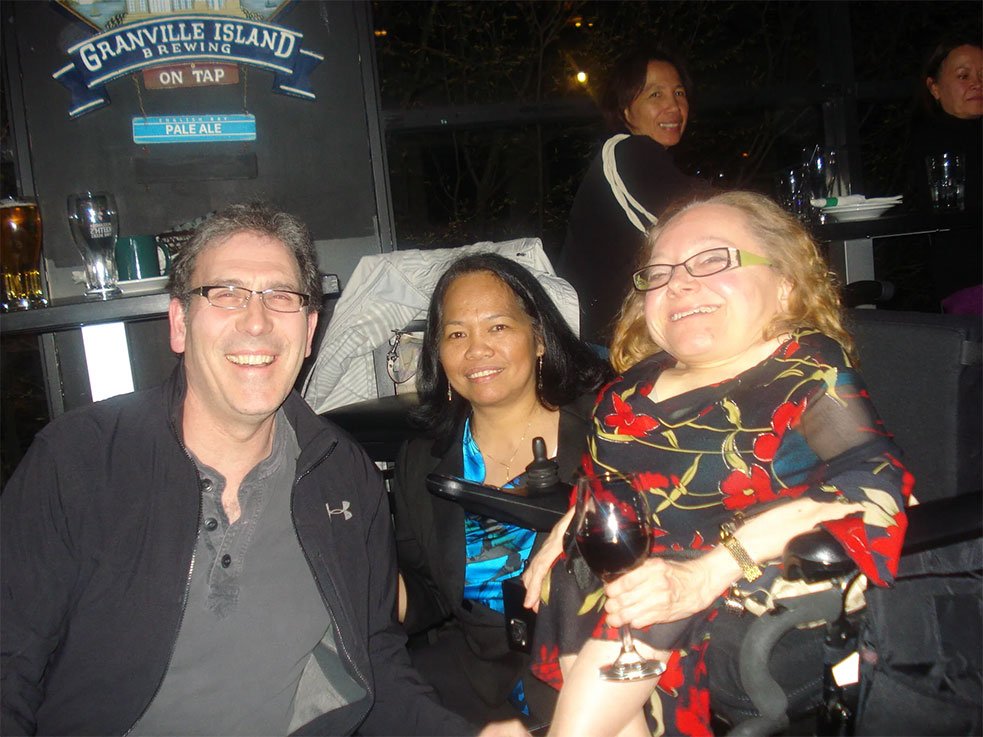 Group of three adults seated together at a fundraising event, chatting and smiling, with drinks on the table in front of them.